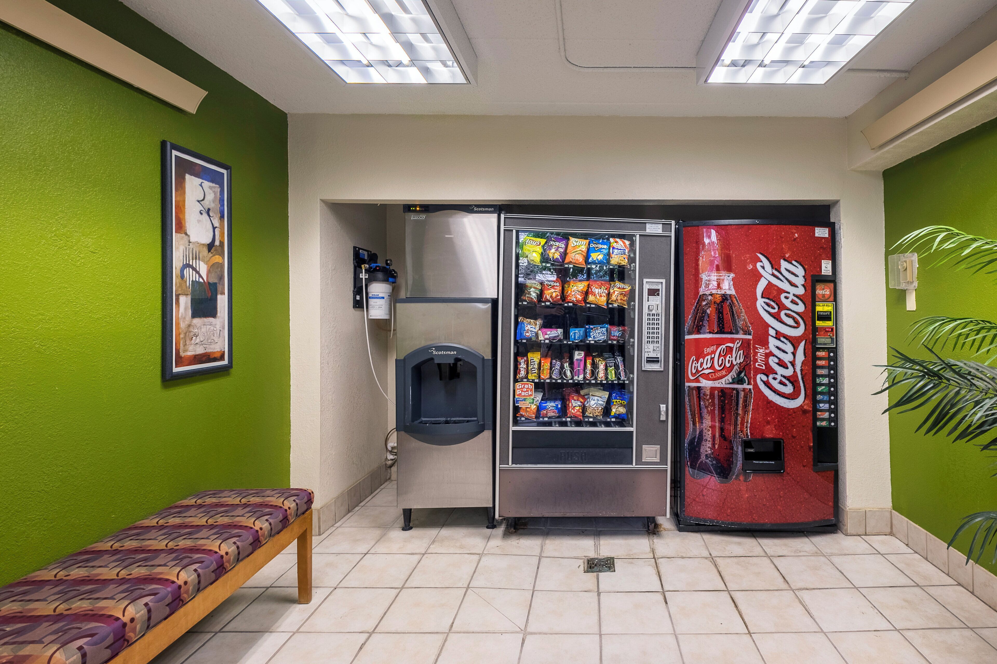 A room with a bench, a water dispenser, a snack vending machine, and a Coca-Cola vending machine.