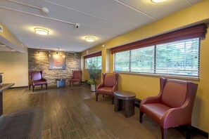 A reception area with stone wall, leather chairs, a small table, and a potted plant. - Red Roof Inn PLUS+ West Springfield (West Springfield)