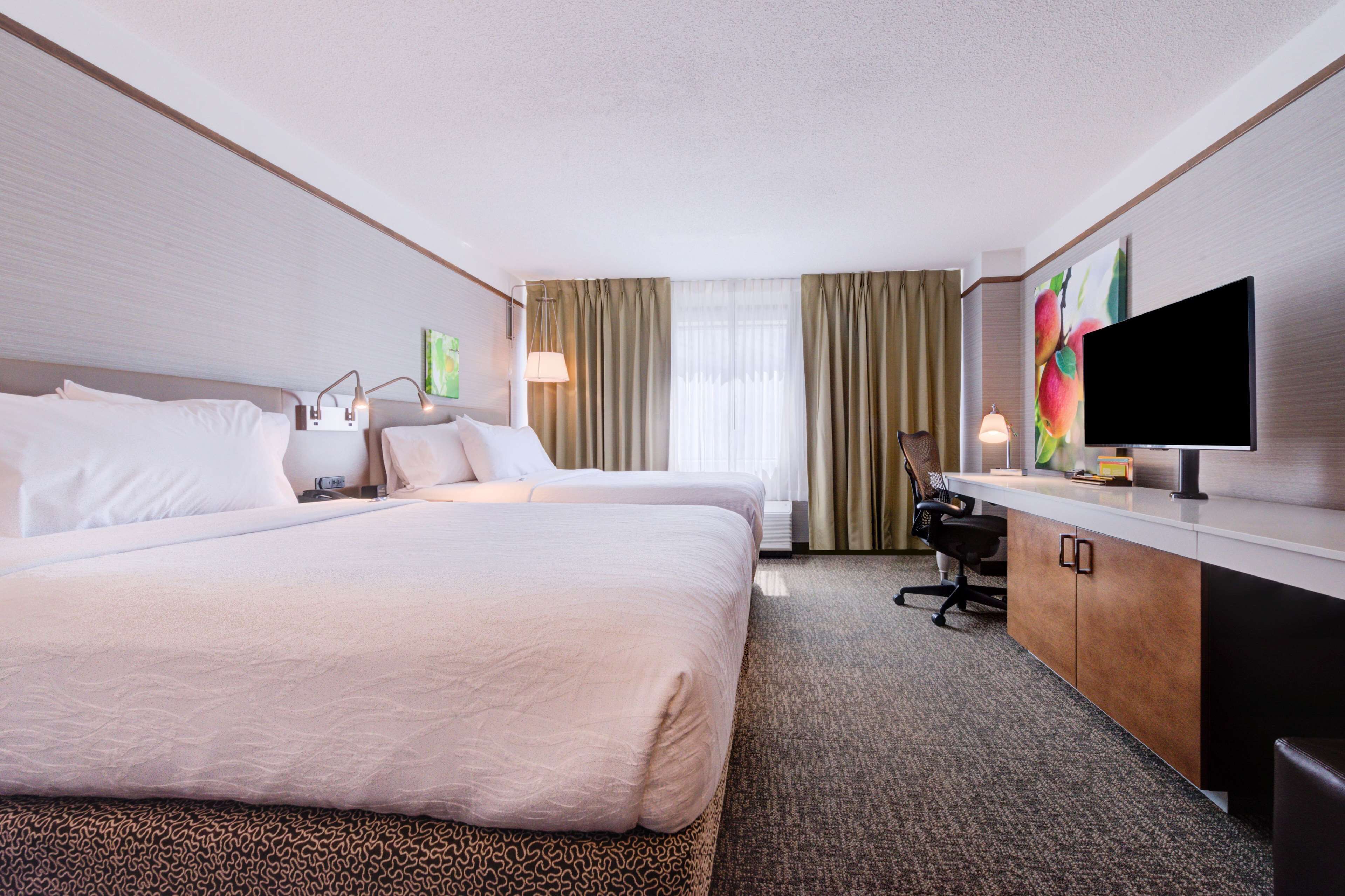 Ein Hotelzimmer mit zwei Betten, einem Schreibtisch, einem Stuhl, einem Fernseher und einem Fenster mit Vorhängen.