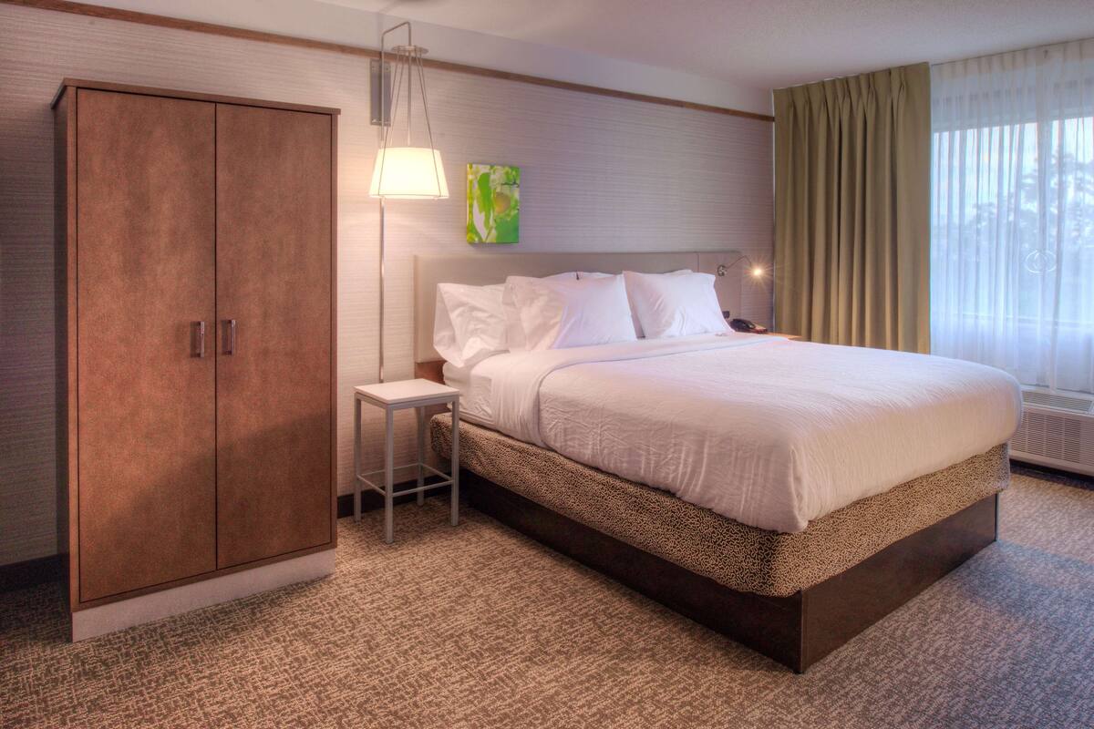 A hotel room with a large bed, a wardrobe, a nightstand, a lamp, and a window with curtains.