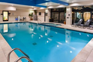 Una piscina interior con agua cristalina, una zona de descanso junto a la piscina y un mostrador de recepción.