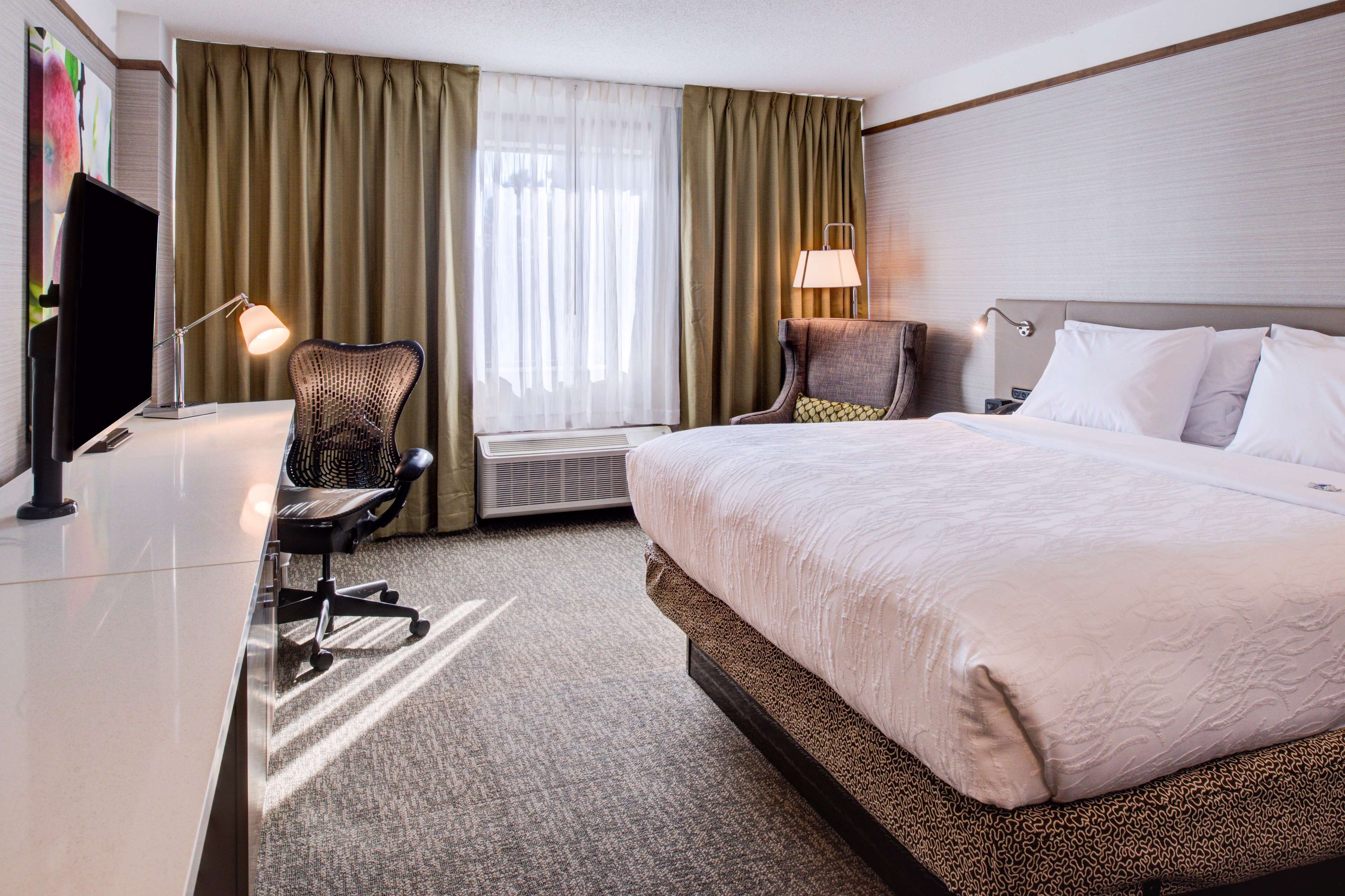 A hotel room with a large bed, a desk with a chair, a television, and a window with curtains.