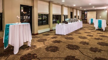 A hotel room with a long corridor lined with tables, large windows, and a patterned carpet.