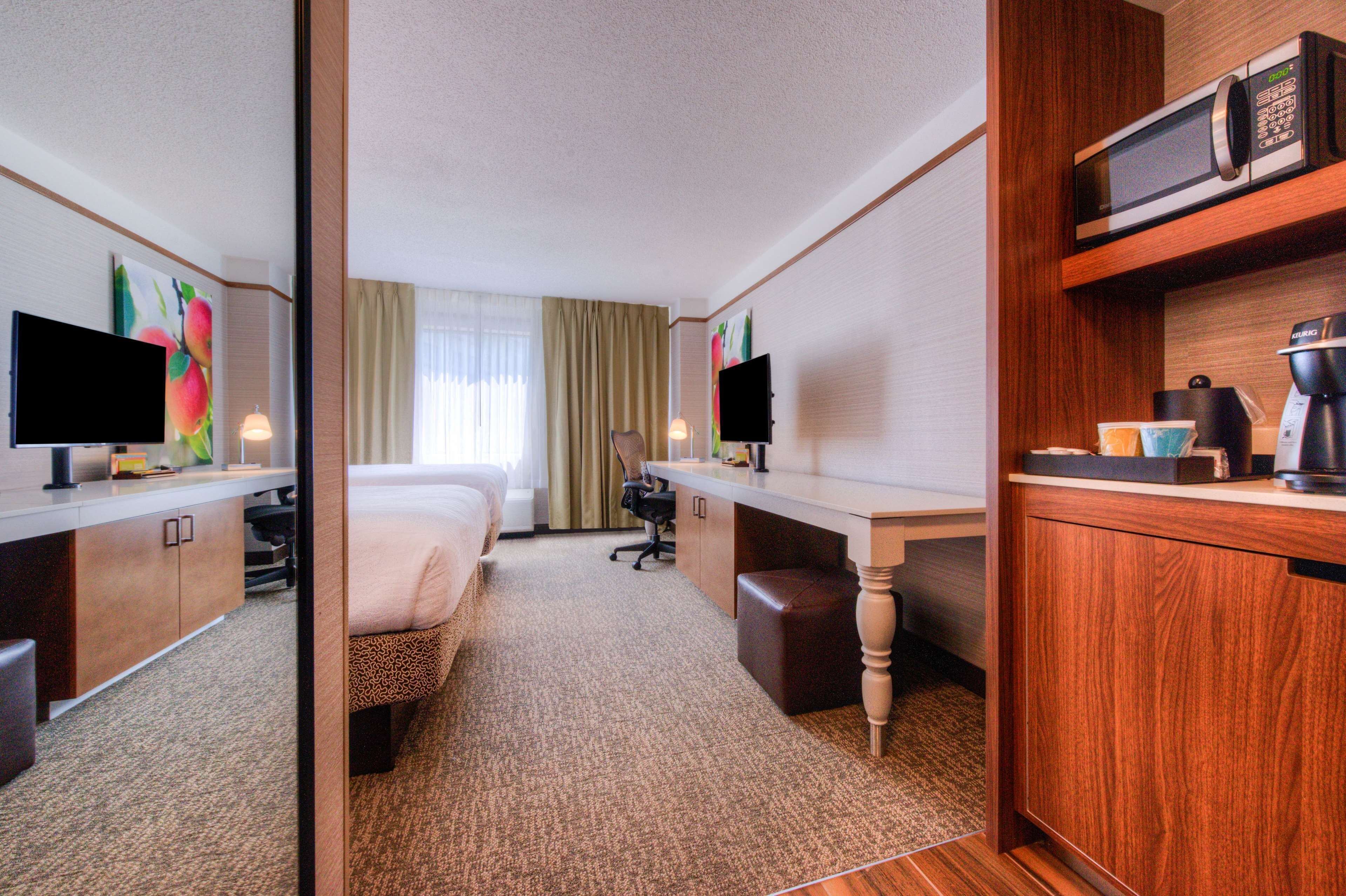 A hotel room with a bed, a desk, a chair, a television, a microwave, and a coffee maker.