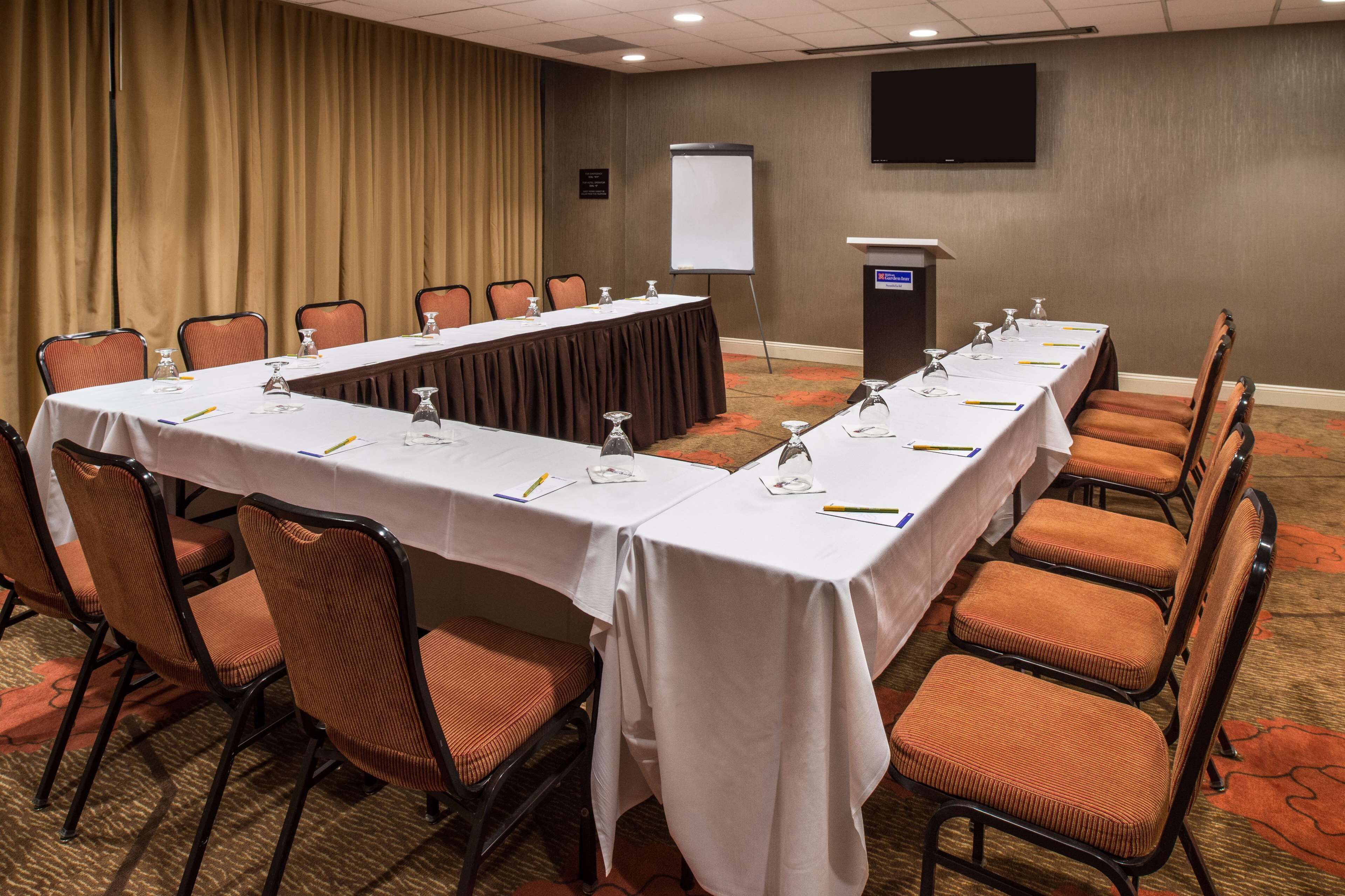 A conference room with a long table, chairs, a podium, and a projector screen.