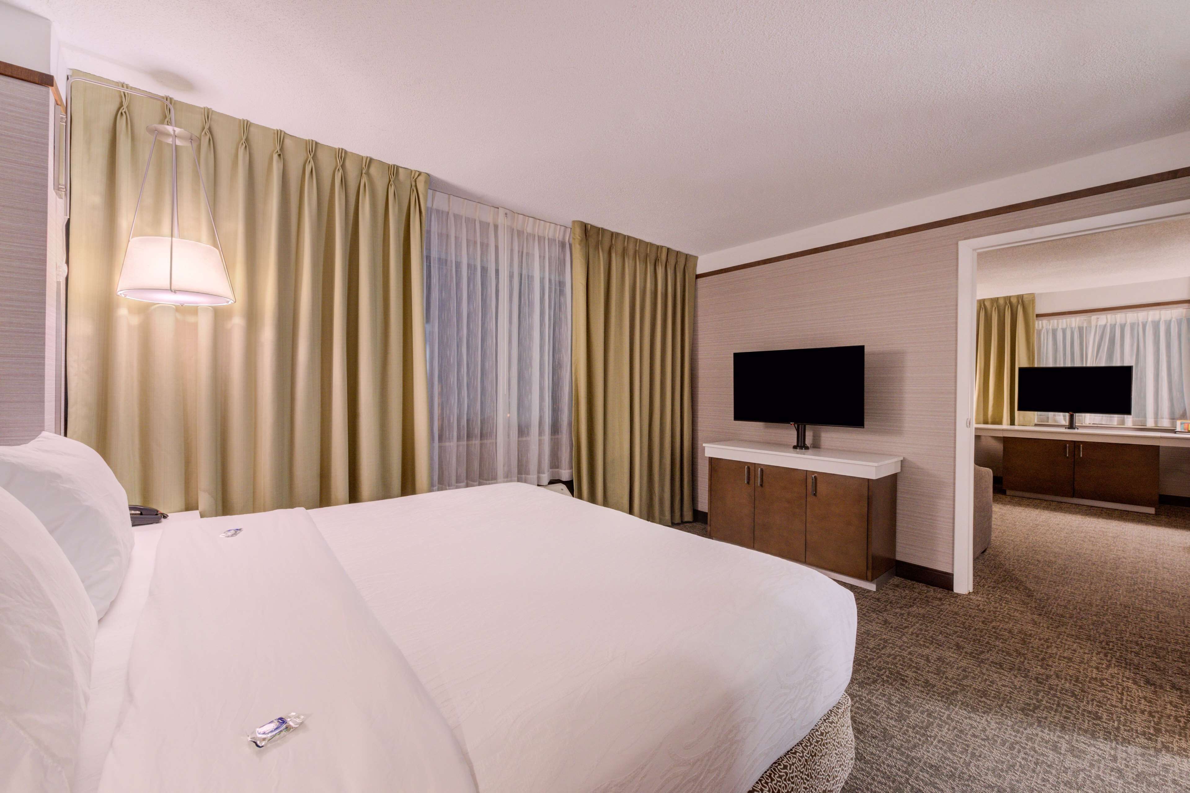 A hotel room with a large bed, a television, a desk, and a mirror.