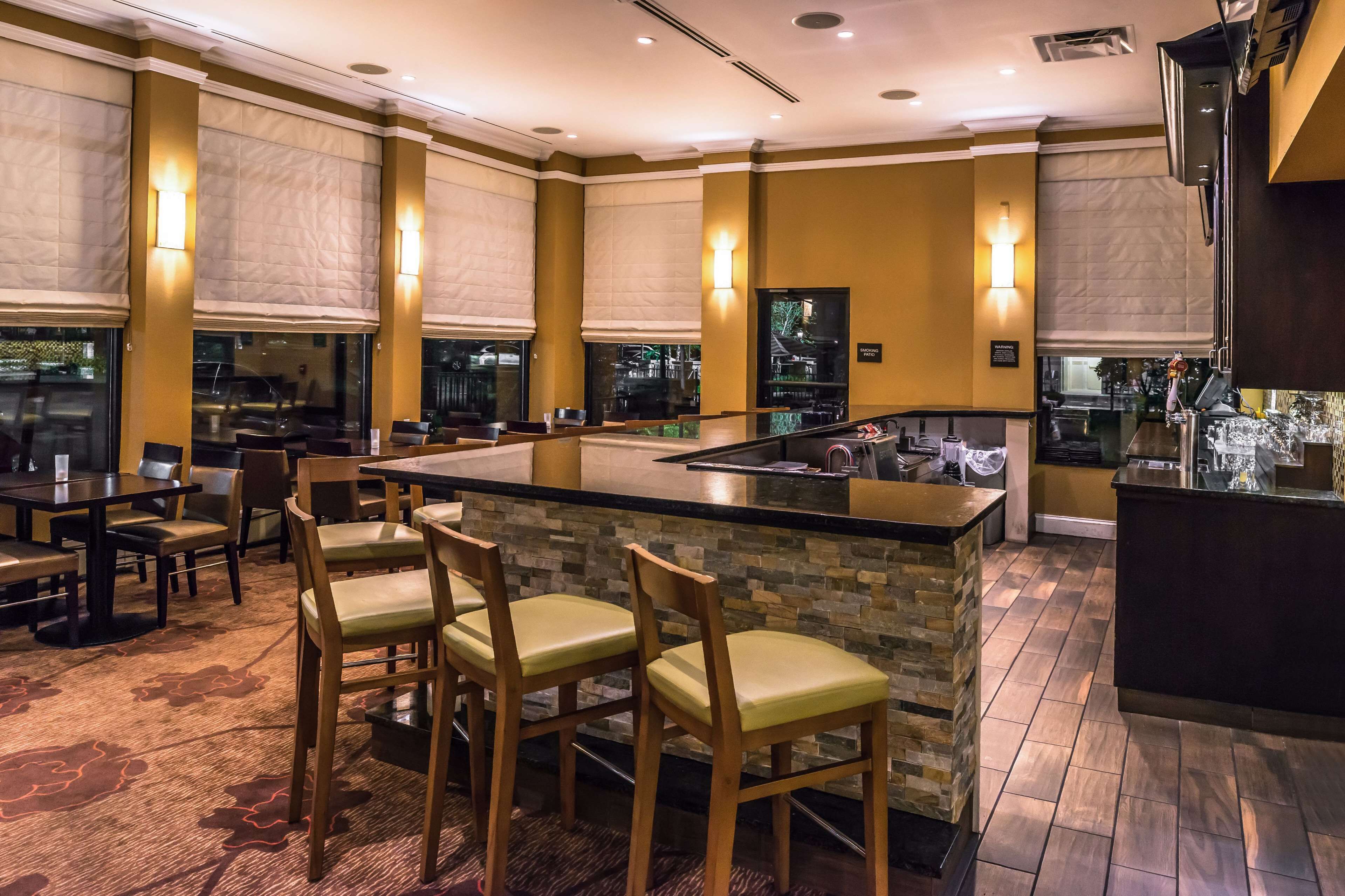 Un restaurante con zona de bar, sillas acolchadas y suelo de baldosas de piedra.
