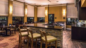 A restaurant with a bar area, cushioned chairs, and a stone-tiled floor.