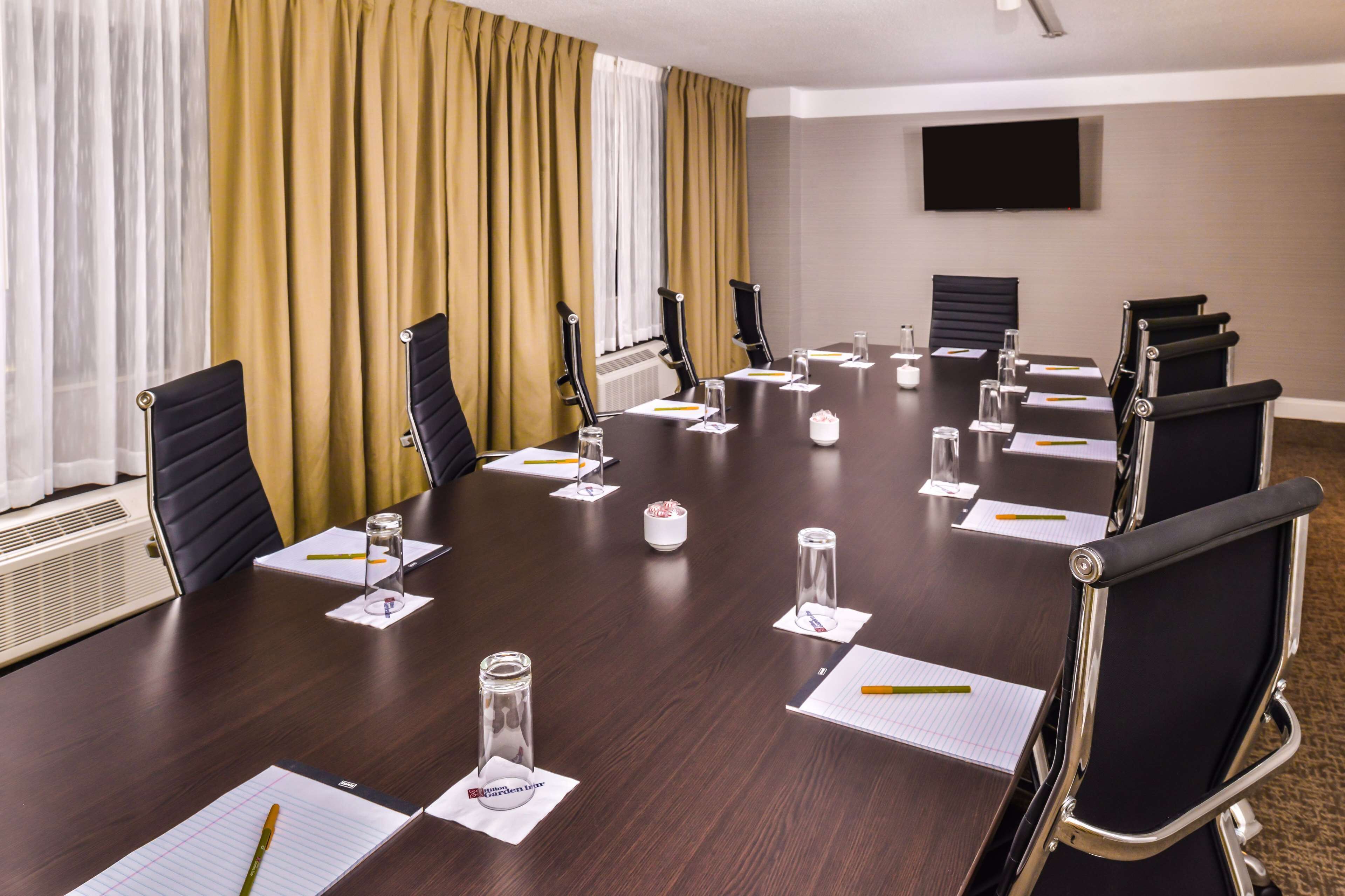 A conference room with a long table, chairs, and a TV screen on the wall.