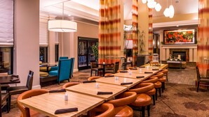 A hotel dining area with long wooden tables and orange leather chairs, a fireplace, and a large painting on the wall.
