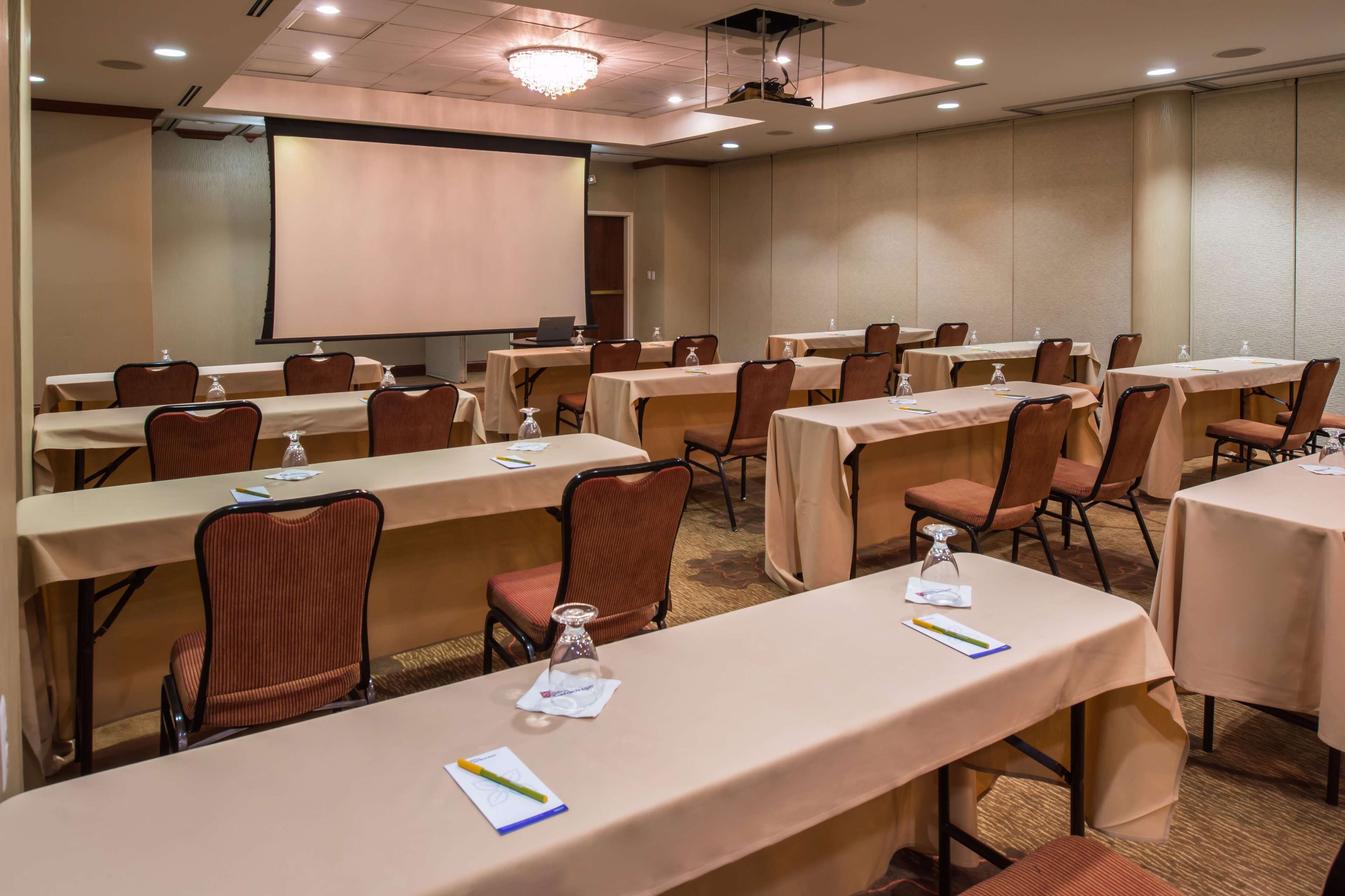A conference room with multiple tables, chairs, and a projector screen.