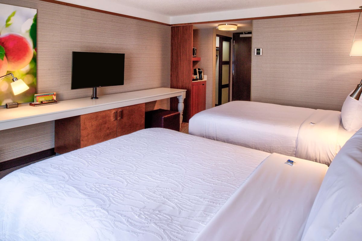 A hotel room with two beds, a TV, a desk, and a mirror.