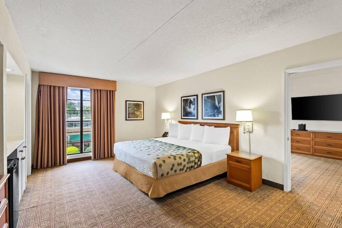 A hotel room with a bed, bedside tables, a TV, and a window with curtains.