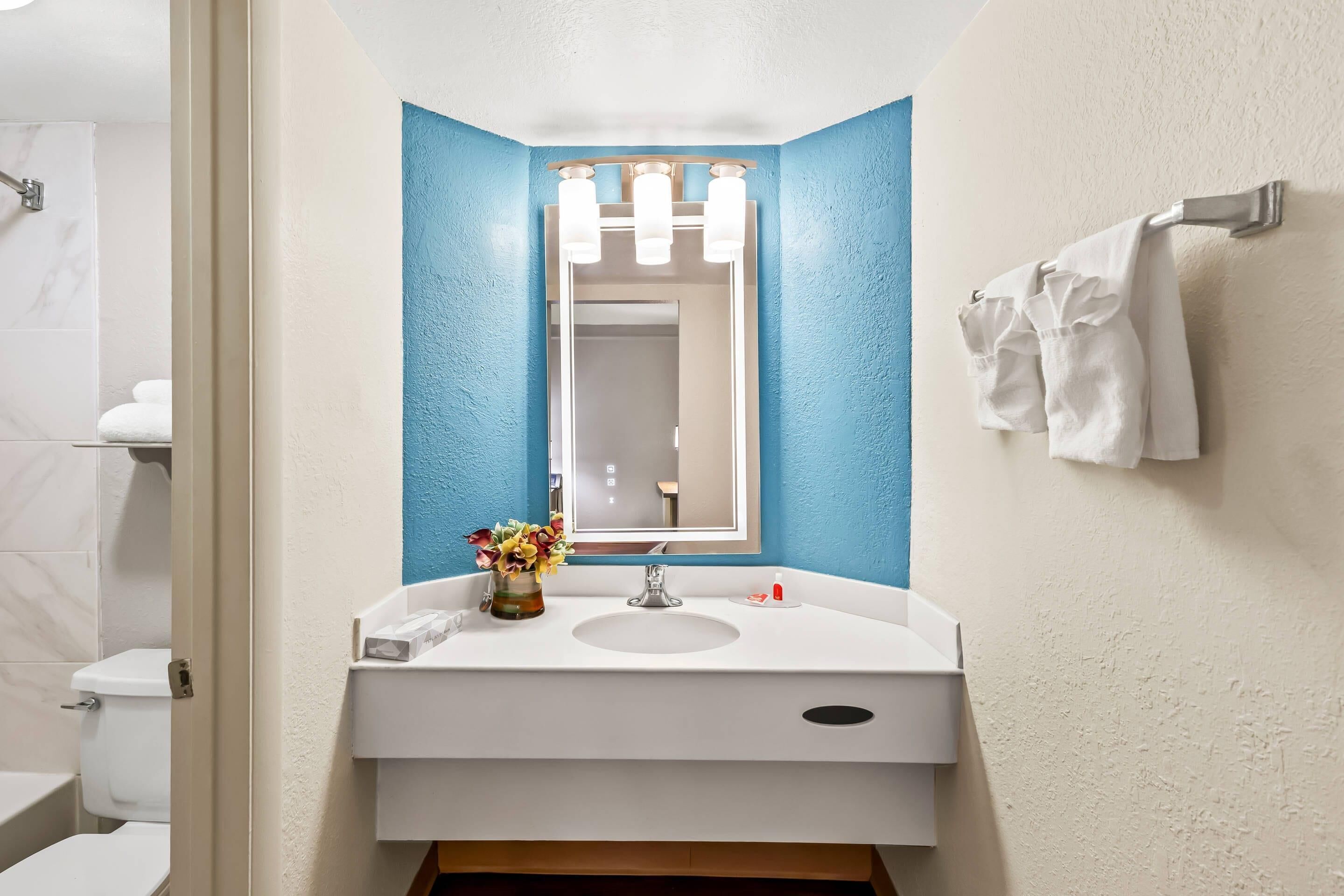 A bathroom with a white sink, a mirror with three lights, and a towel rack with towels.