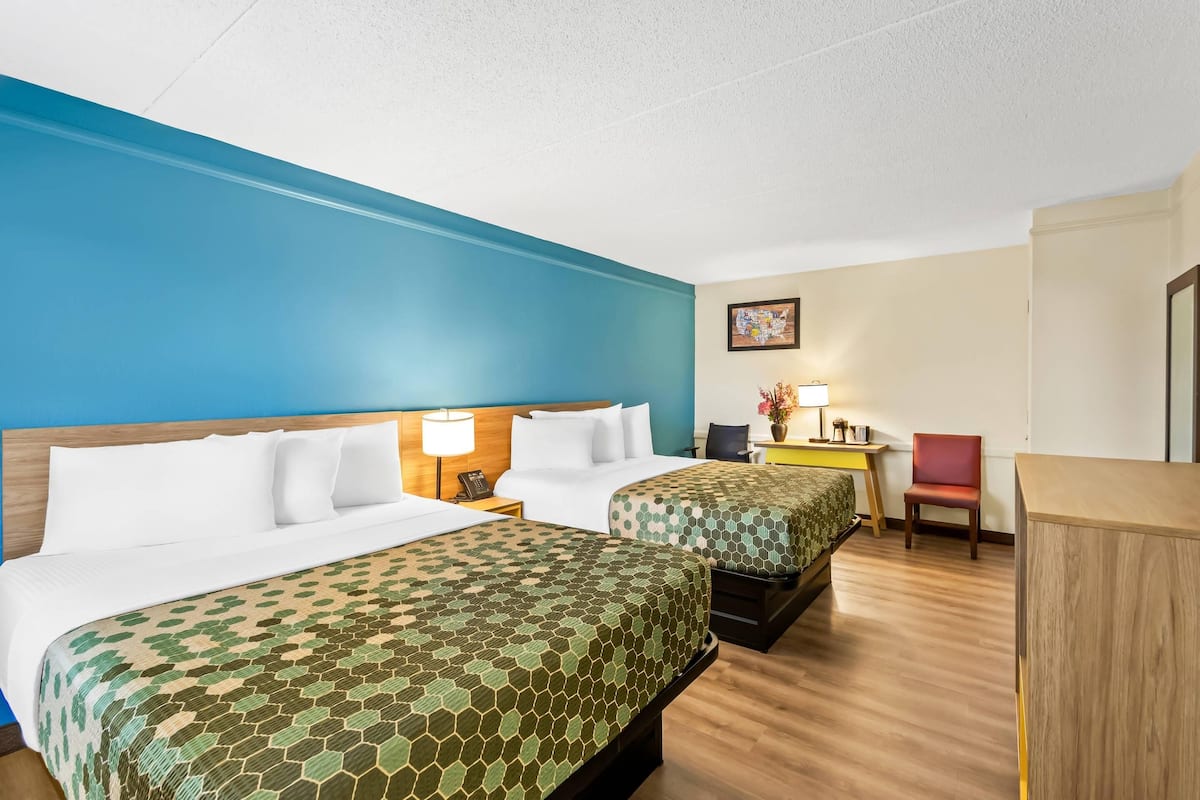 A hotel room with two beds, a desk, a chair, and a lamp.
