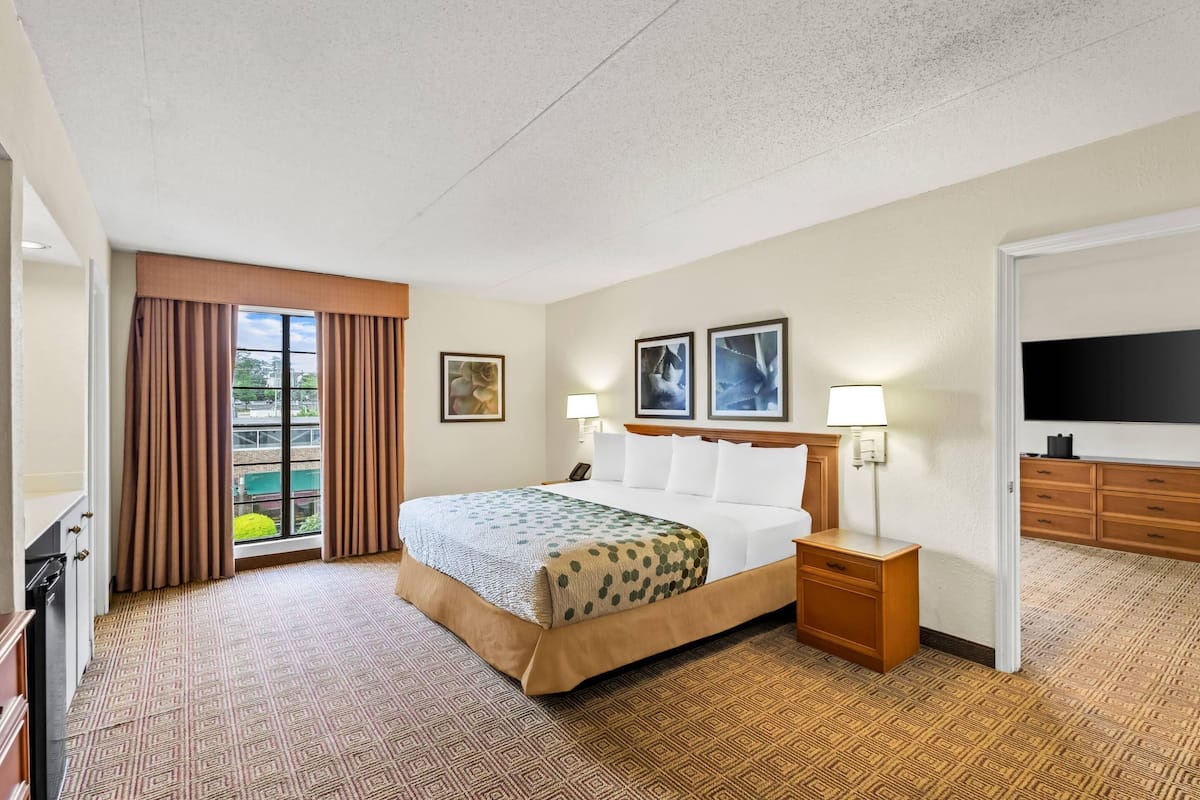 A hotel room with a large bed, a TV, a desk, and a window with curtains.