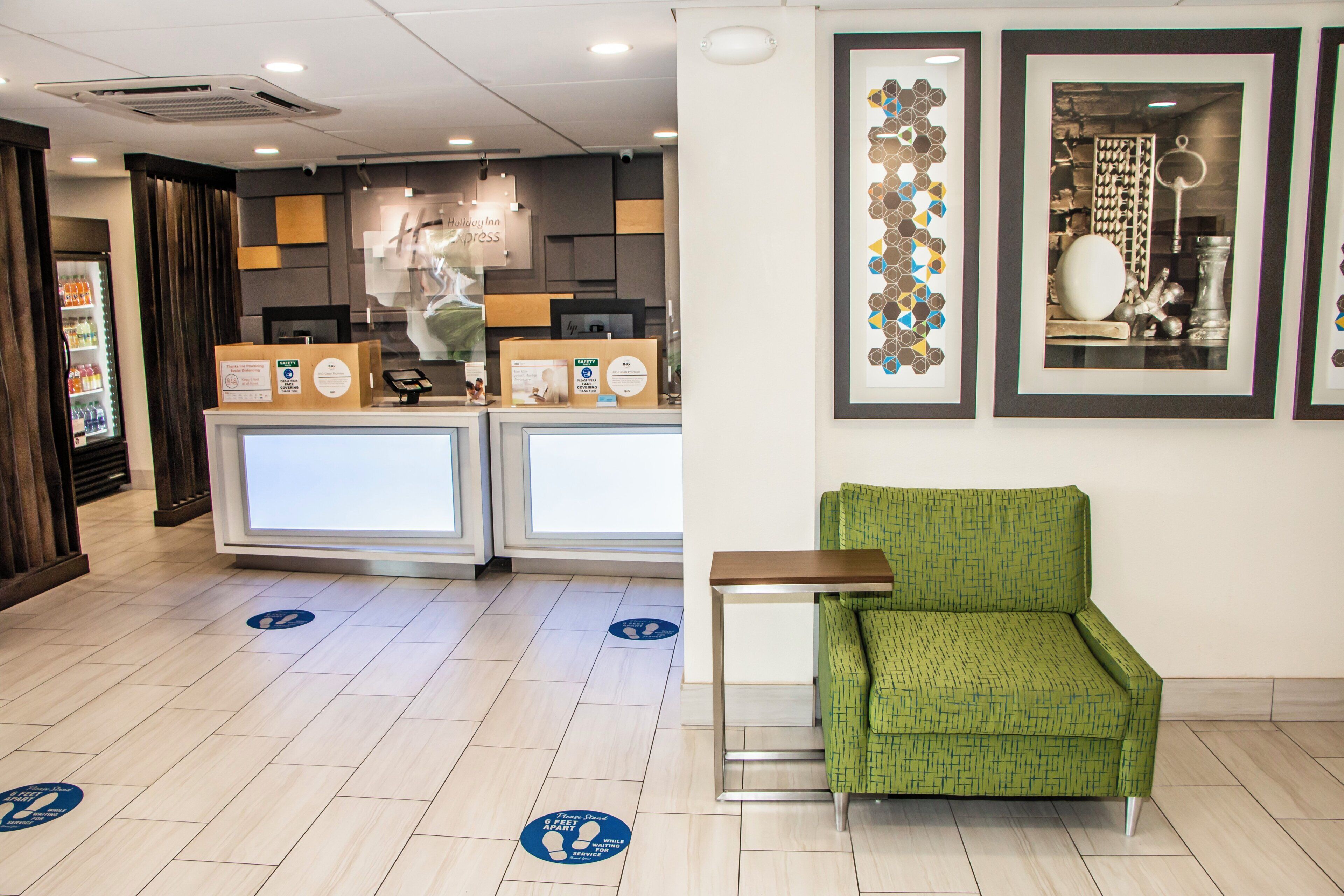 A hotel reception area with a green armchair, a counter with a computer, and framed artwork on the wall.