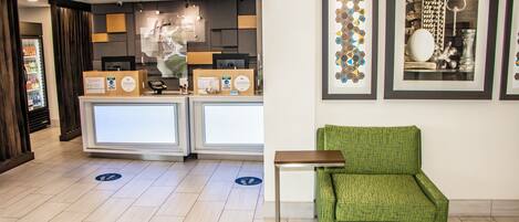 A hotel reception area with a green armchair, a counter with a computer, and framed artwork on the wall.