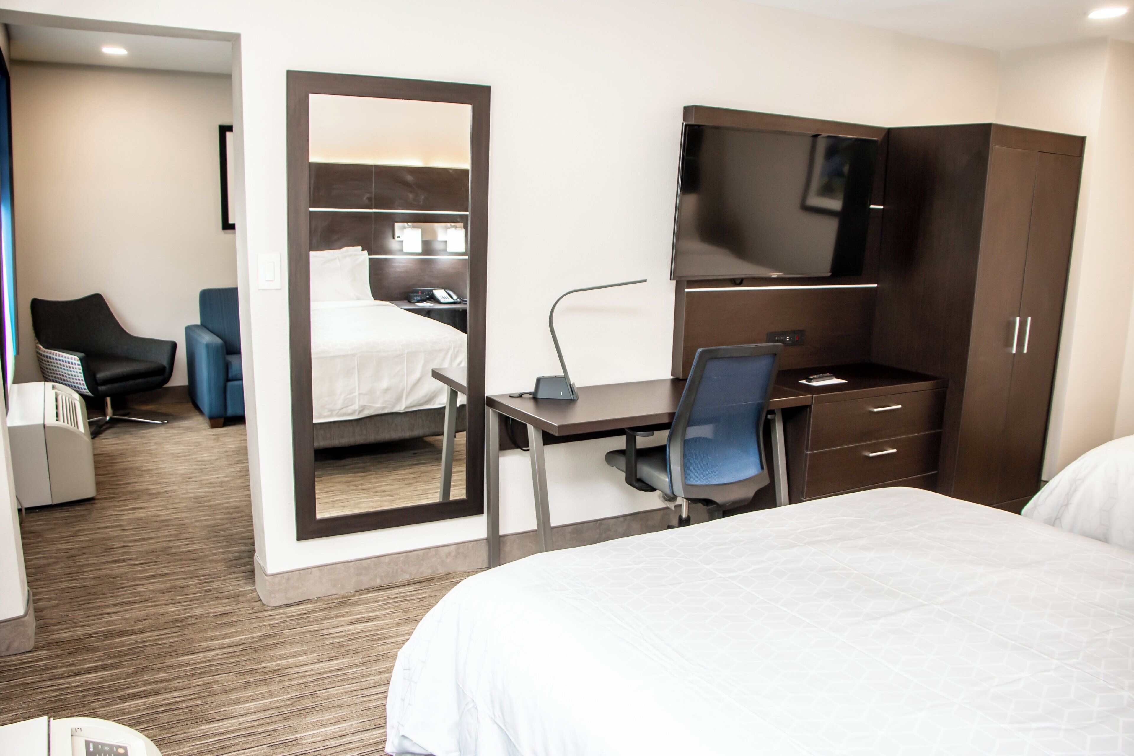 Quarto de hotel com cama, escrivaninha, cadeira, televisão e guarda-roupa.