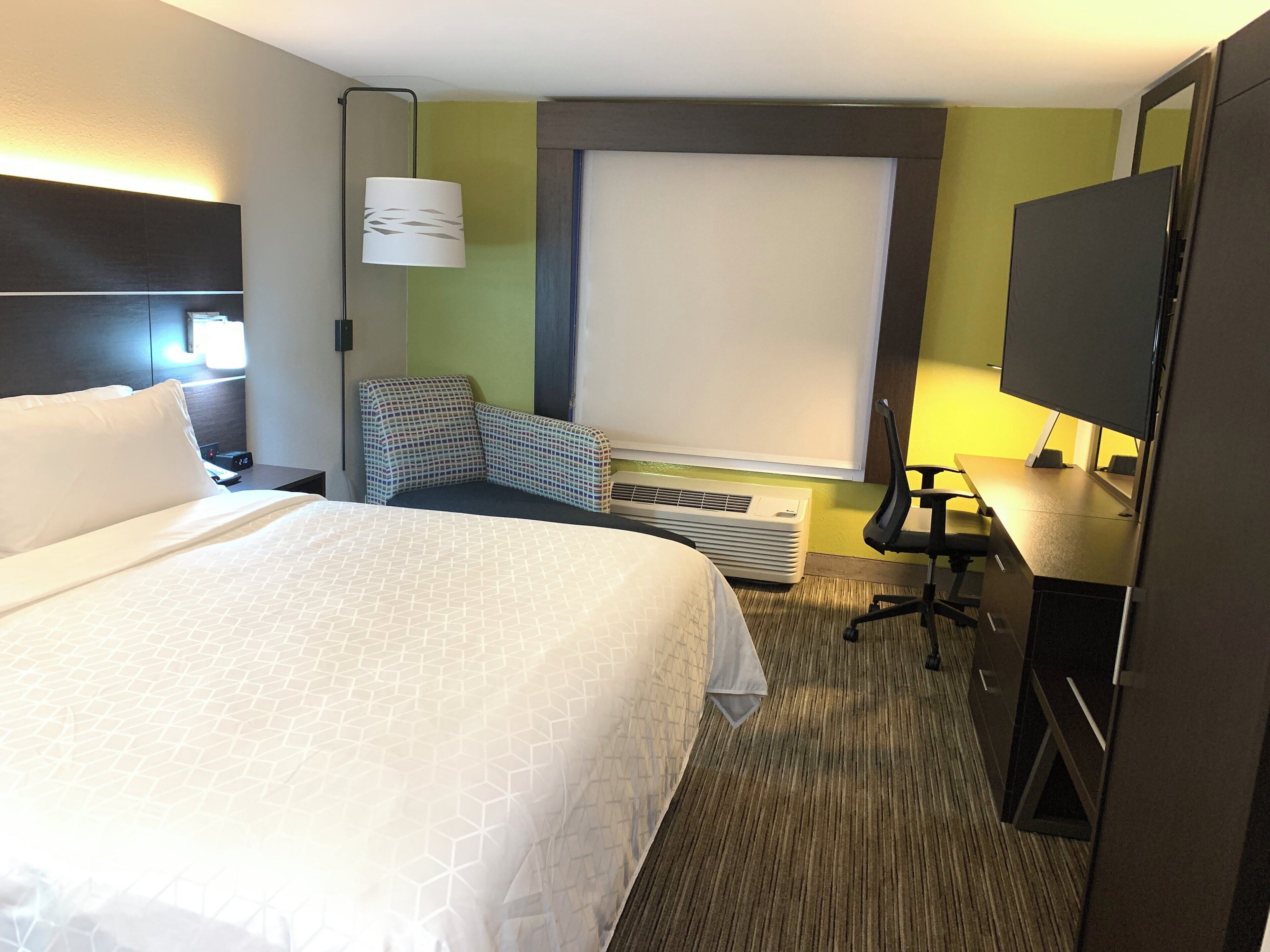 Una habitación de hotel con una cama grande, un escritorio con silla, un televisor y una ventana.