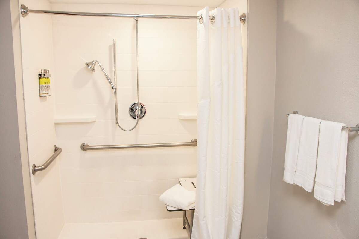 A bathroom with a shower, grab bars, a towel rack, and a toilet.