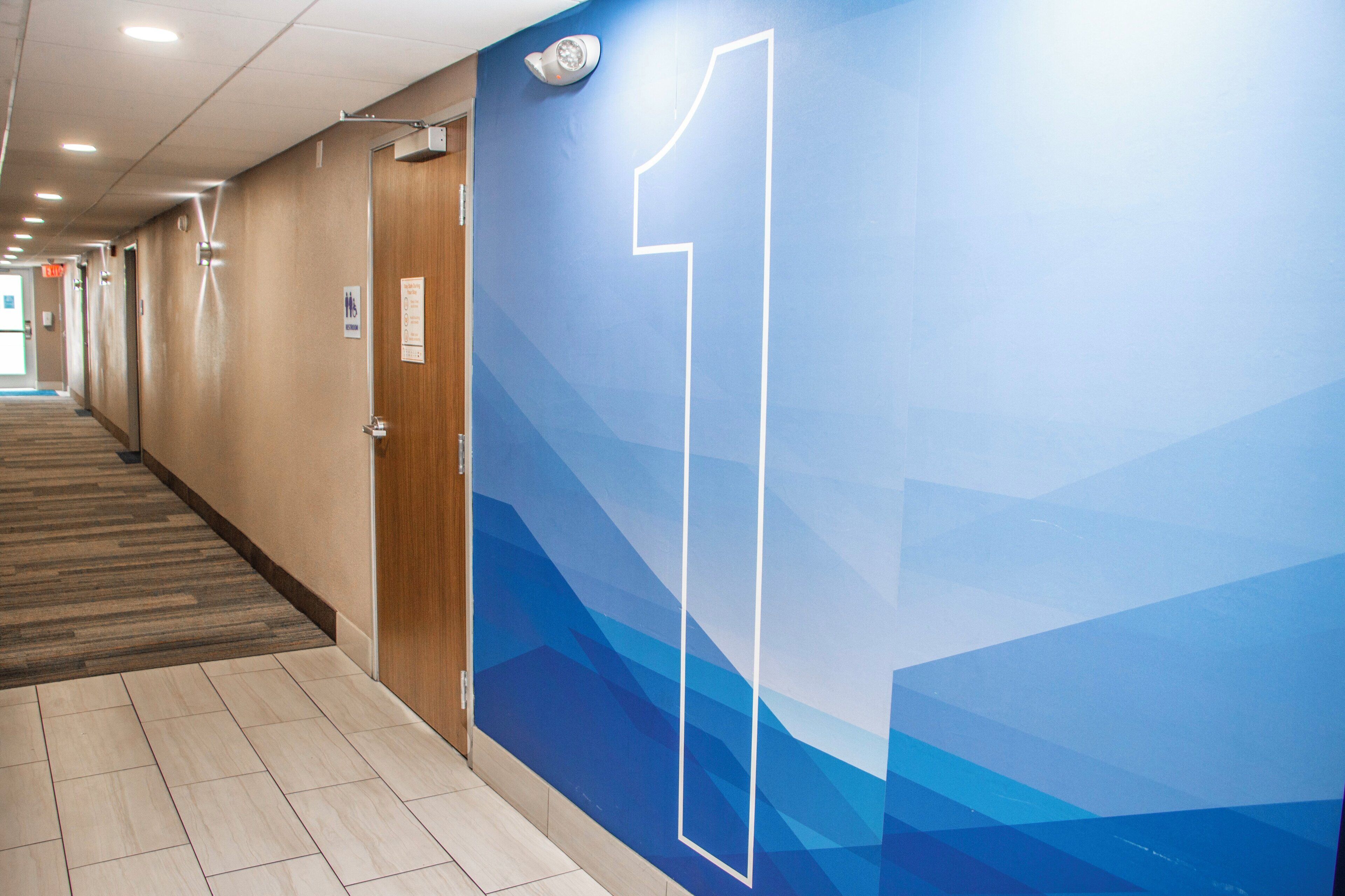 A hotel corridor with a blue wall featuring a large number '1' sign, wooden doors, and a tiled floor.