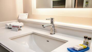 A hotel bathroom with a white sink, a mirror above it, and toiletries on the counter.