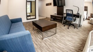A modern hotel room with a blue sofa, a wooden coffee table, a desk with a chair, a flat-screen TV, and a large mirror. - Holiday Inn Express Allentown North by IHG (Allentown)