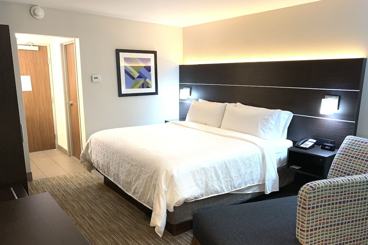 Una habitación de hotel con cama, mesita de noche, silla y un cuadro en la pared.