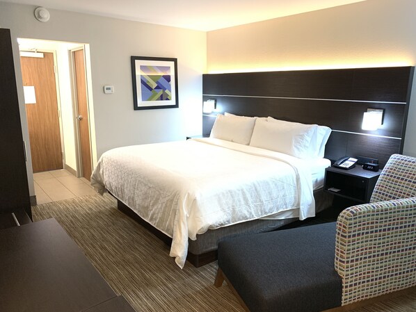 Una habitación de hotel con cama, mesita de noche, silla y un cuadro en la pared.