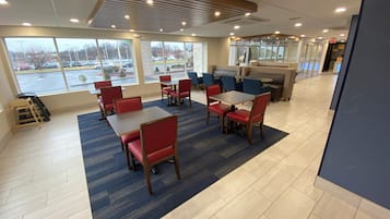 A restaurant with tables and chairs, large windows, and a view of a parking lot.