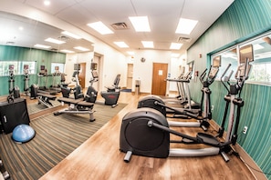 Un gimnasio con diverso equipo de ejercicio, incluyendo cintas de correr y bicicletas estáticas, y una pared de espejos.