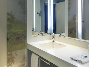 Un baño con un lavabo blanco, dos llaves y un espejo grande.