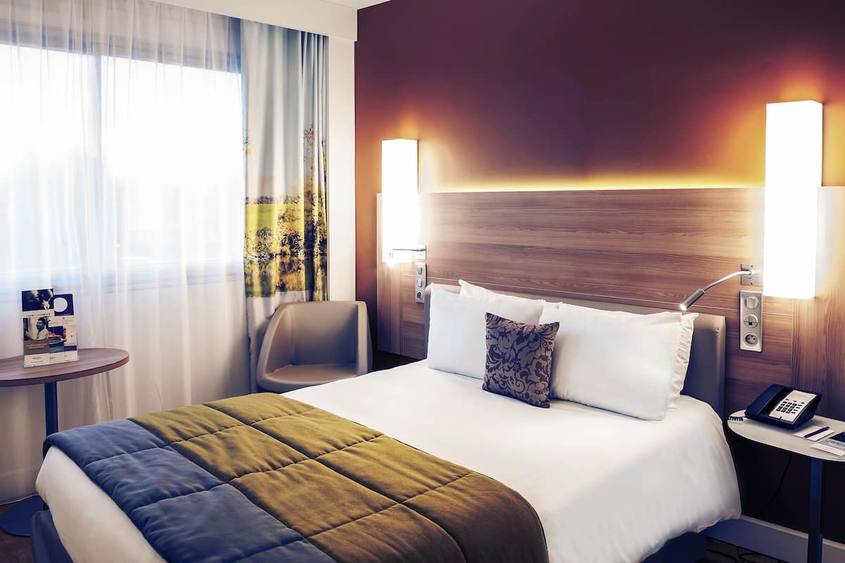 A hotel room with a large bed, two bedside lamps, a small table with a phone, and a chair.