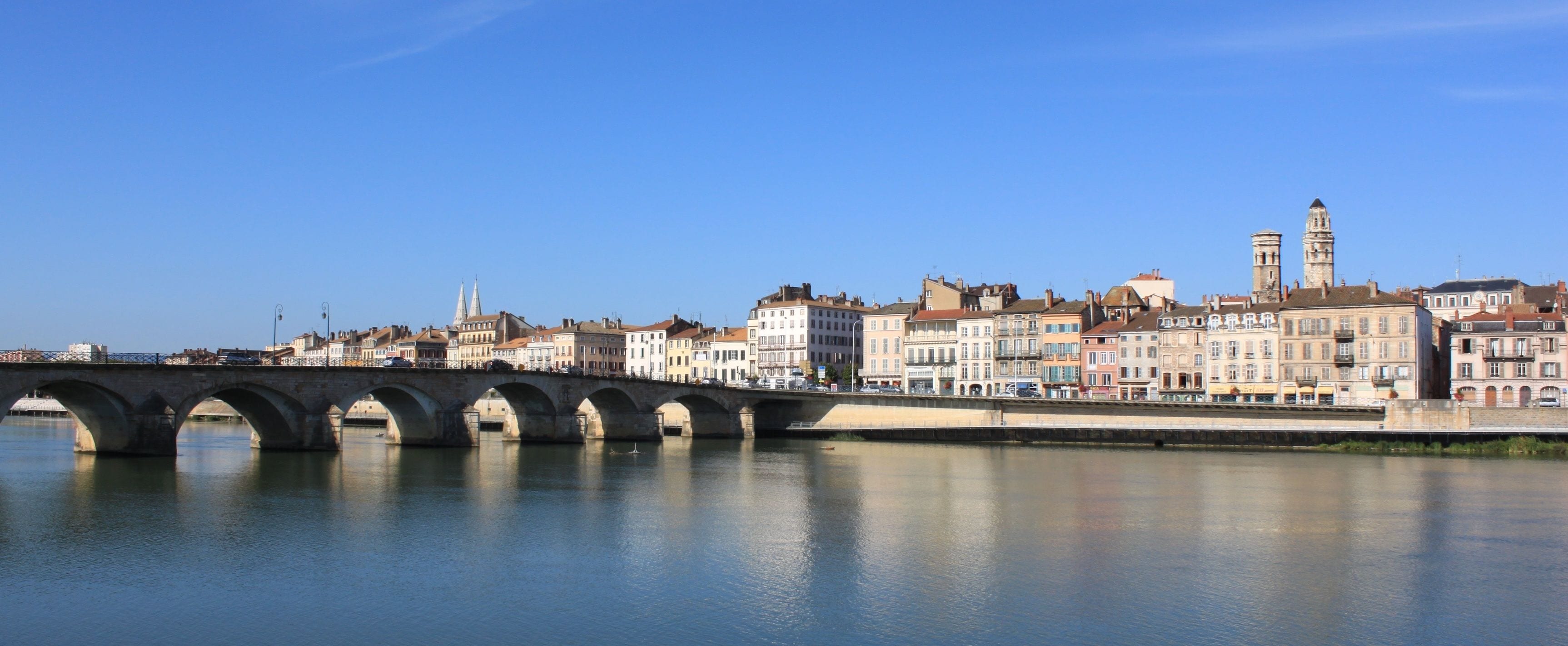 A stone bridge over a calm river with historic buildings on the opposite bank.