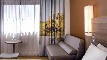 A hotel room with a bed, a sofa, a small table, and a lamp.