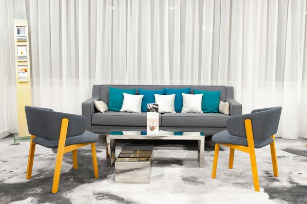 Una sala de estar moderna con un sofá gris, cojines turquesa y dos sillones grises. Un florero con flores y un libro están sobre la mesa de centro frente al sofá.