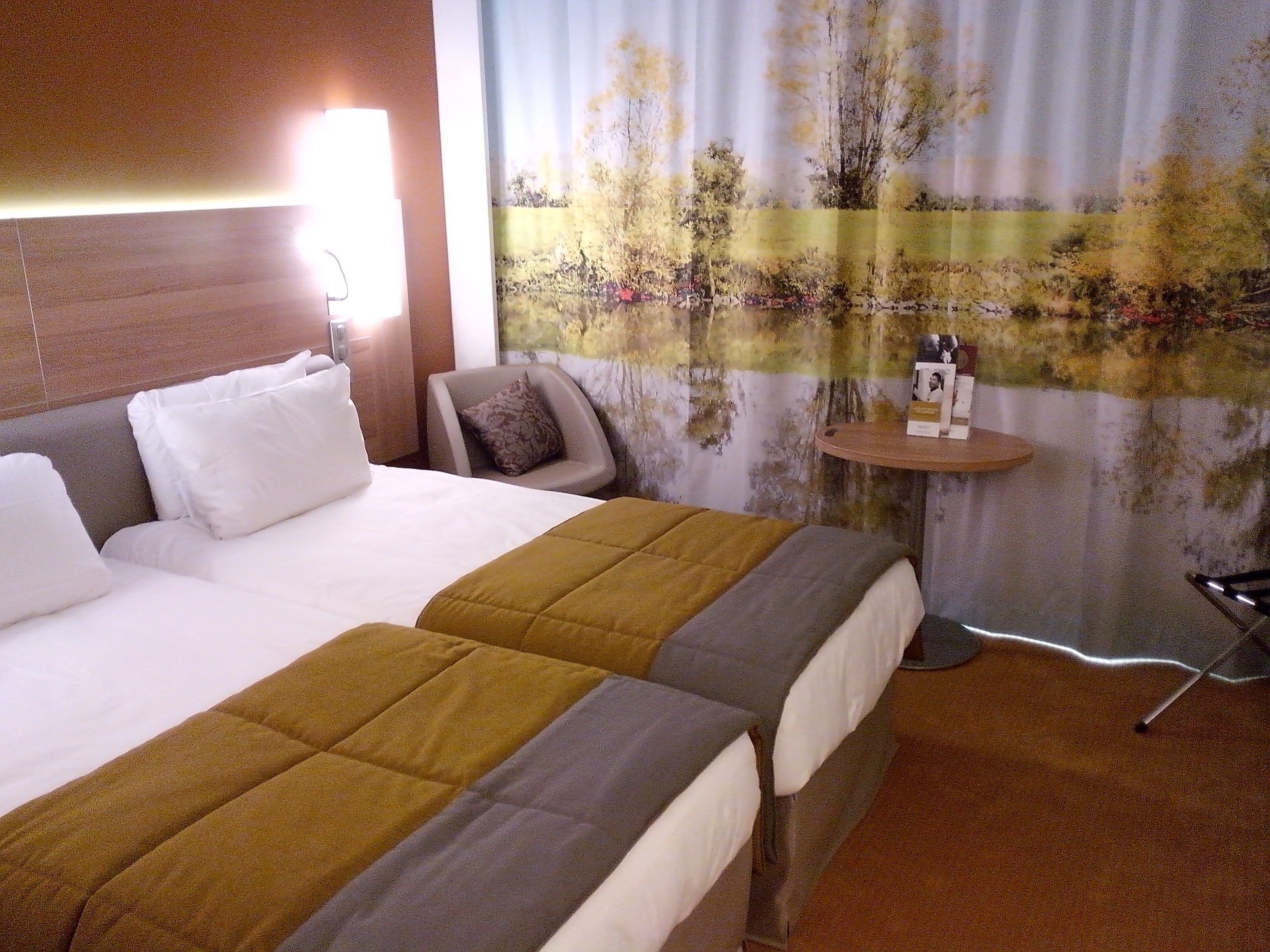 A hotel room with a large bed, two bedside tables, a chair, and a wall with a nature-themed mural.