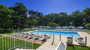 Une piscine avec des chaises longues, une pelouse et une vue sur des arbres et une étendue d’eau.