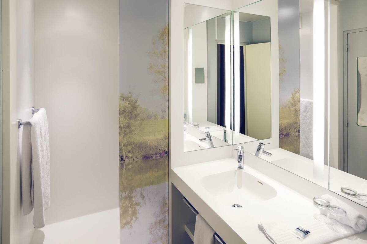 Une salle de bain moderne avec un grand miroir, deux lavabos et un espace douche.