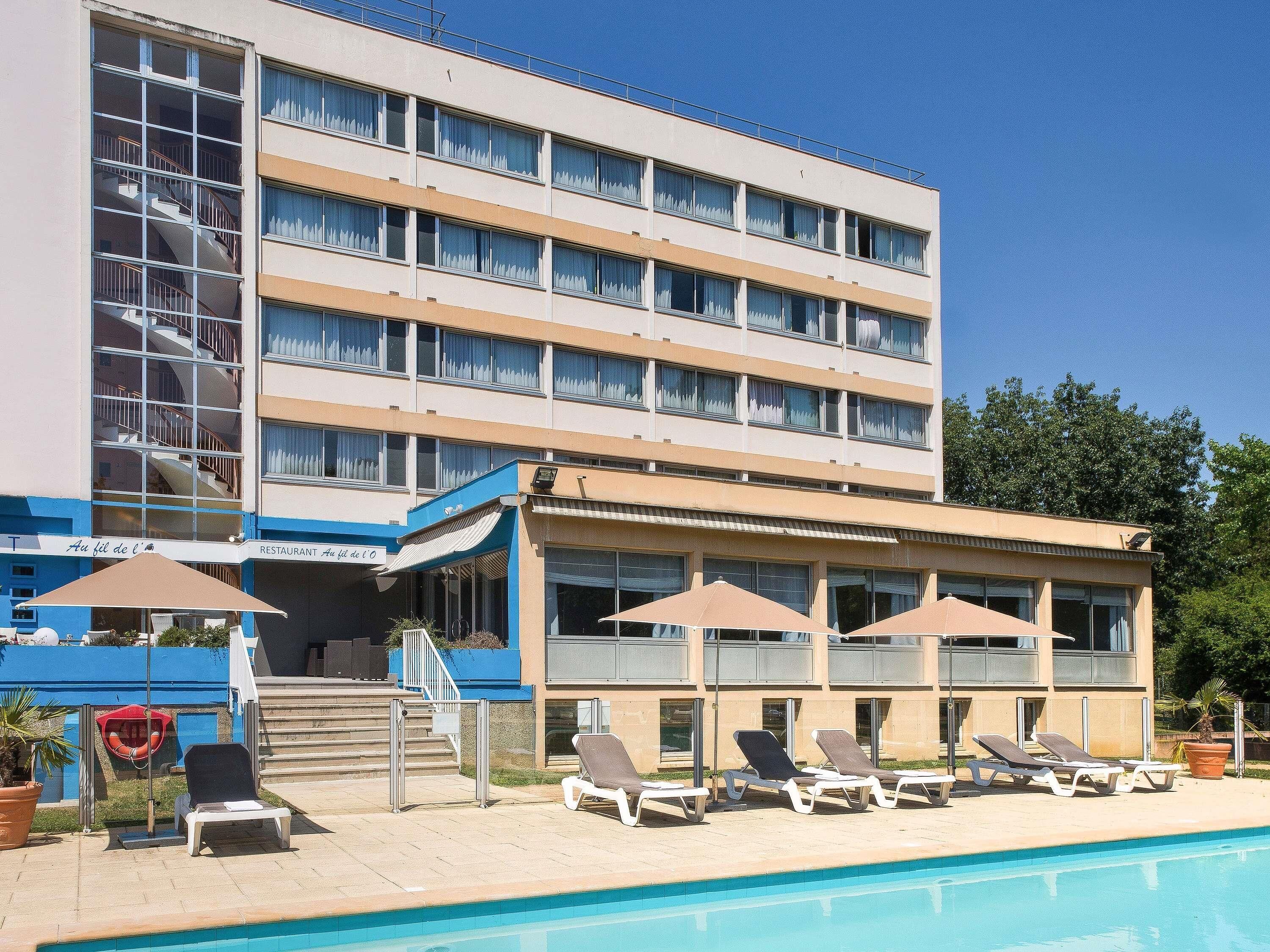 Un hotel con zona de piscina, que incluye sillas de descanso y sombrillas, y una escalera que lleva al edificio.
