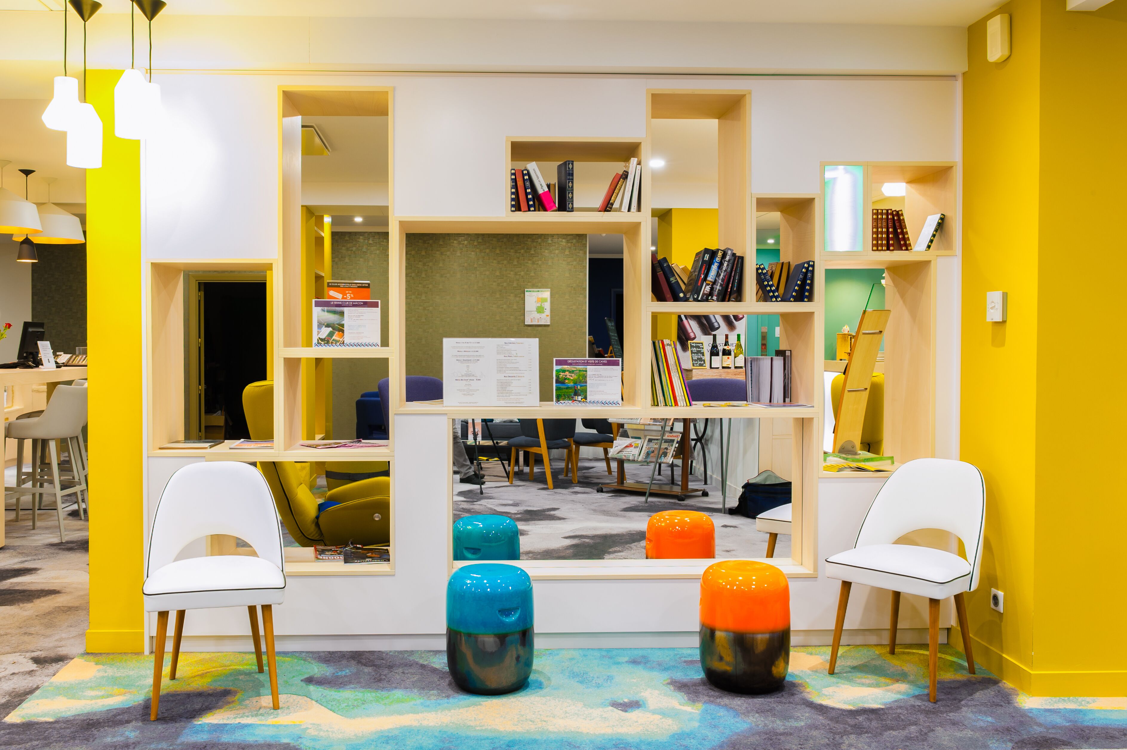 Een helder verlicht leeshoekje met een centrale tafel, stoelen en een boekenplank vol boeken.