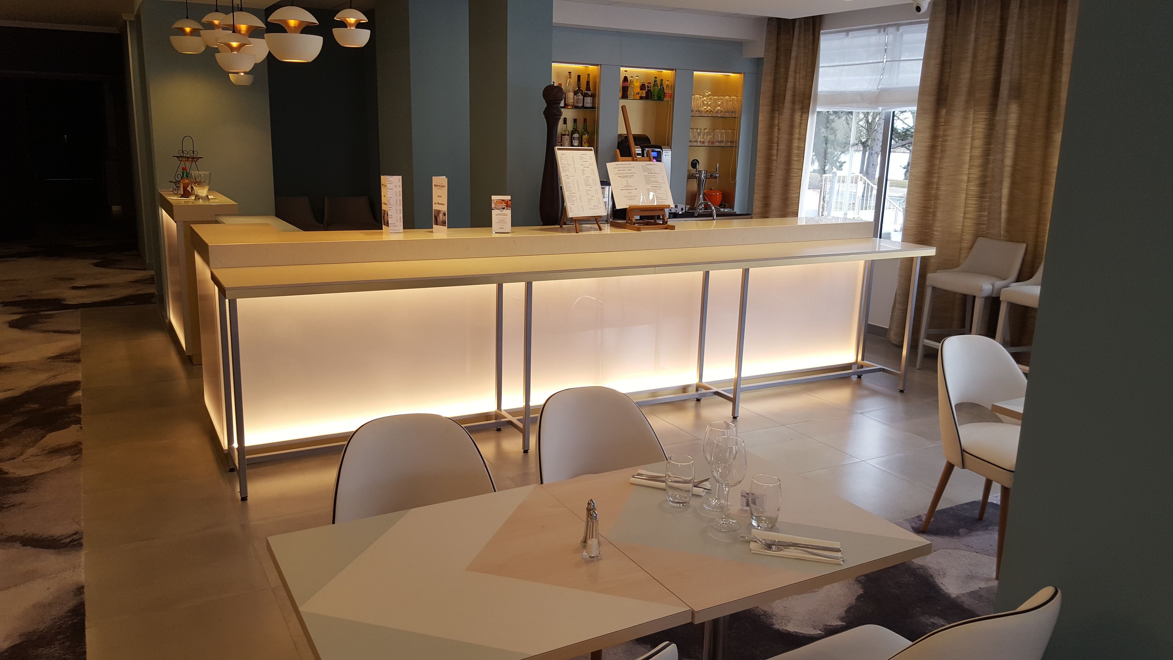 A modern bar area with a long counter, multiple seating options, and a menu board.