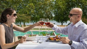 Une table à manger avec une salade, des verres à vin, et une piscine en arrière-plan.