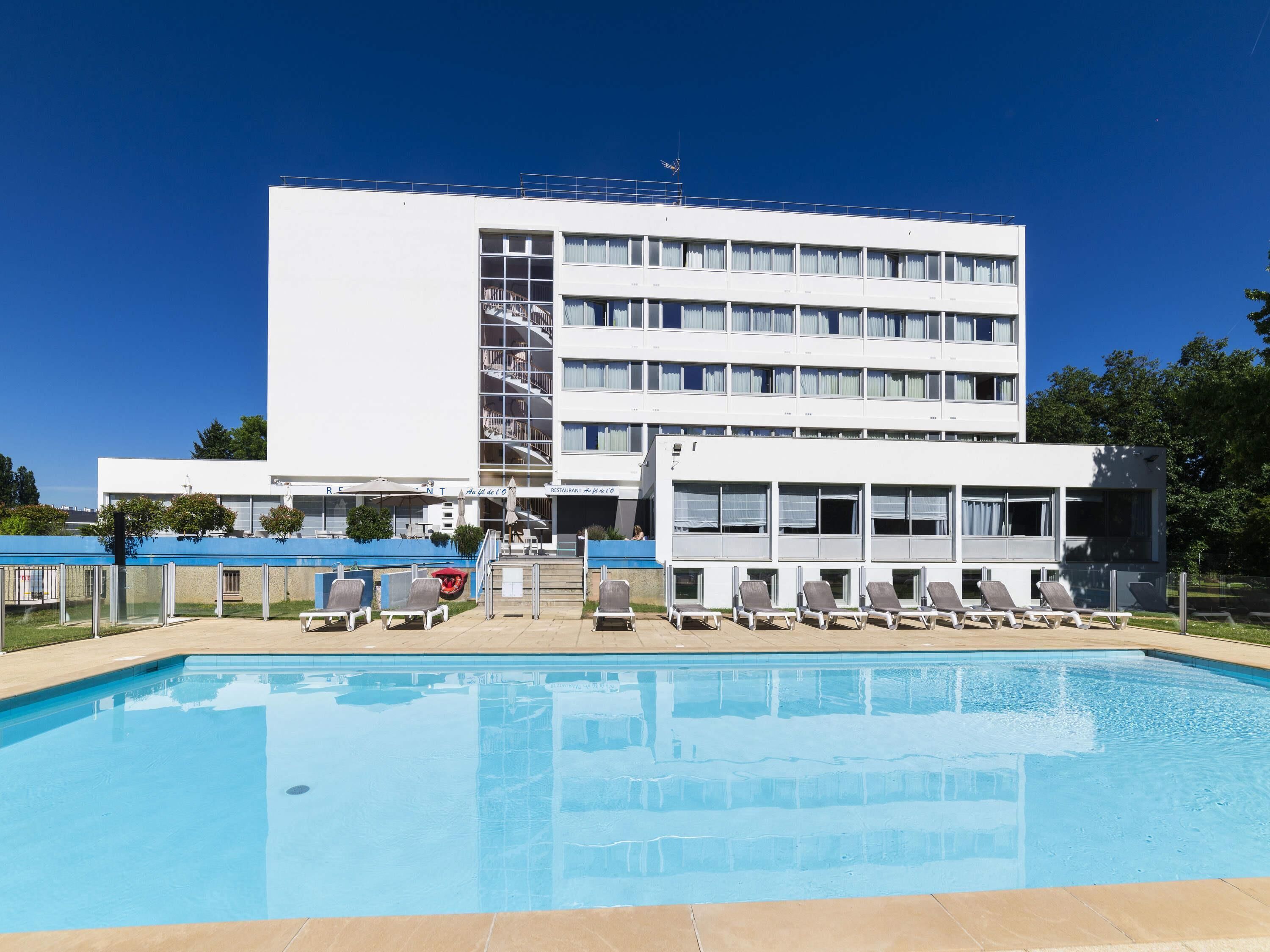 Un hotel moderno con piscina, varios balcones y un restaurante.
