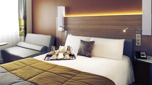 Une chambre d’hôtel comprenant un lit, un canapé, une table de chevet avec une lampe, un téléphone et un plateau avec des articles pour le petit-déjeuner.