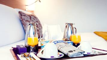 Ein Frühstücksbrettchen mit Orangensaft, Kaffee und einer Zeitung auf einem Hotelbett.