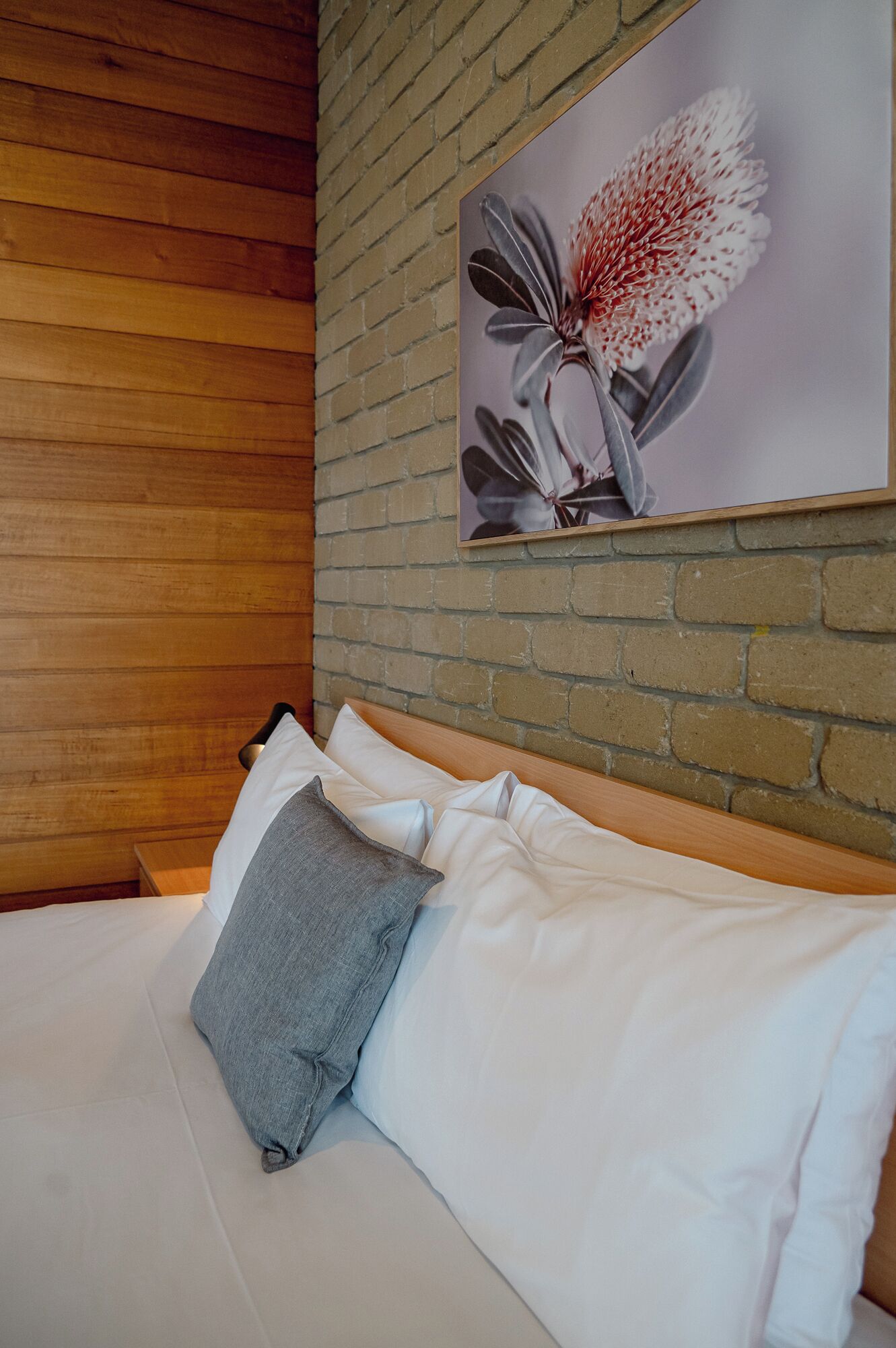 A neatly made bed with white and gray pillows, a wooden headboard, and a brick wall.