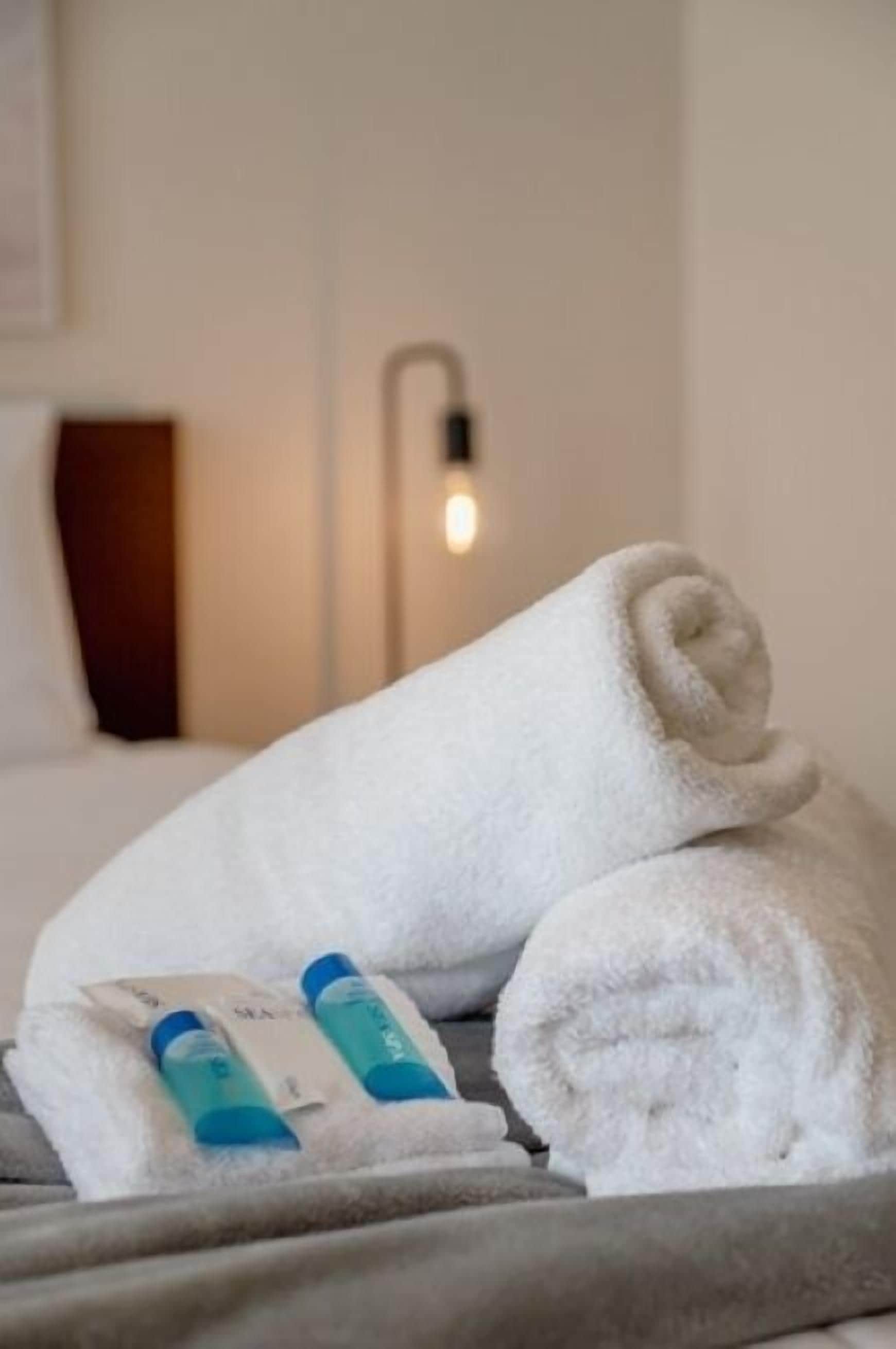 A neatly made bed with a rolled white towel and two toiletry bottles on it.