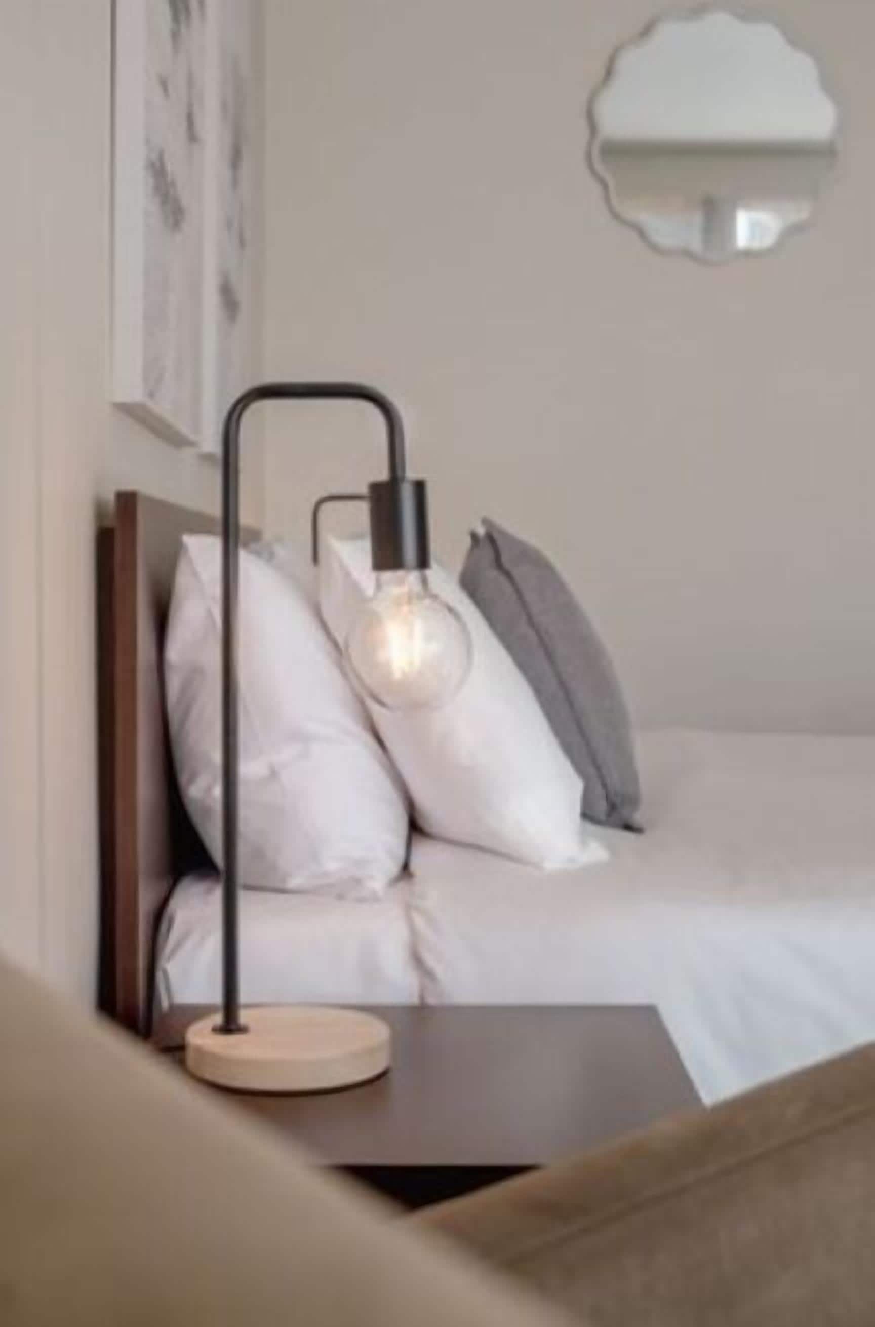 A neatly made bed with white bedding, a bedside table with a lamp, and a wall-mounted light fixture.